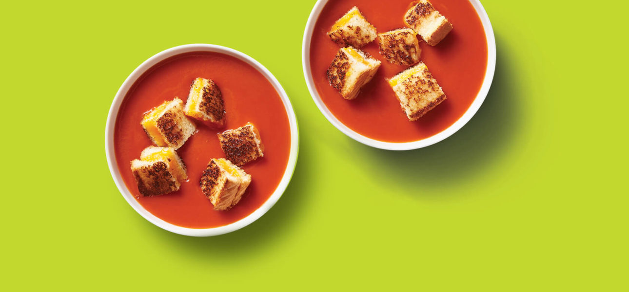 Two bowls of vibrant classic rich red tomato soup topped with squares of perfectly crisped grilled cheese, all for under ten dollars.